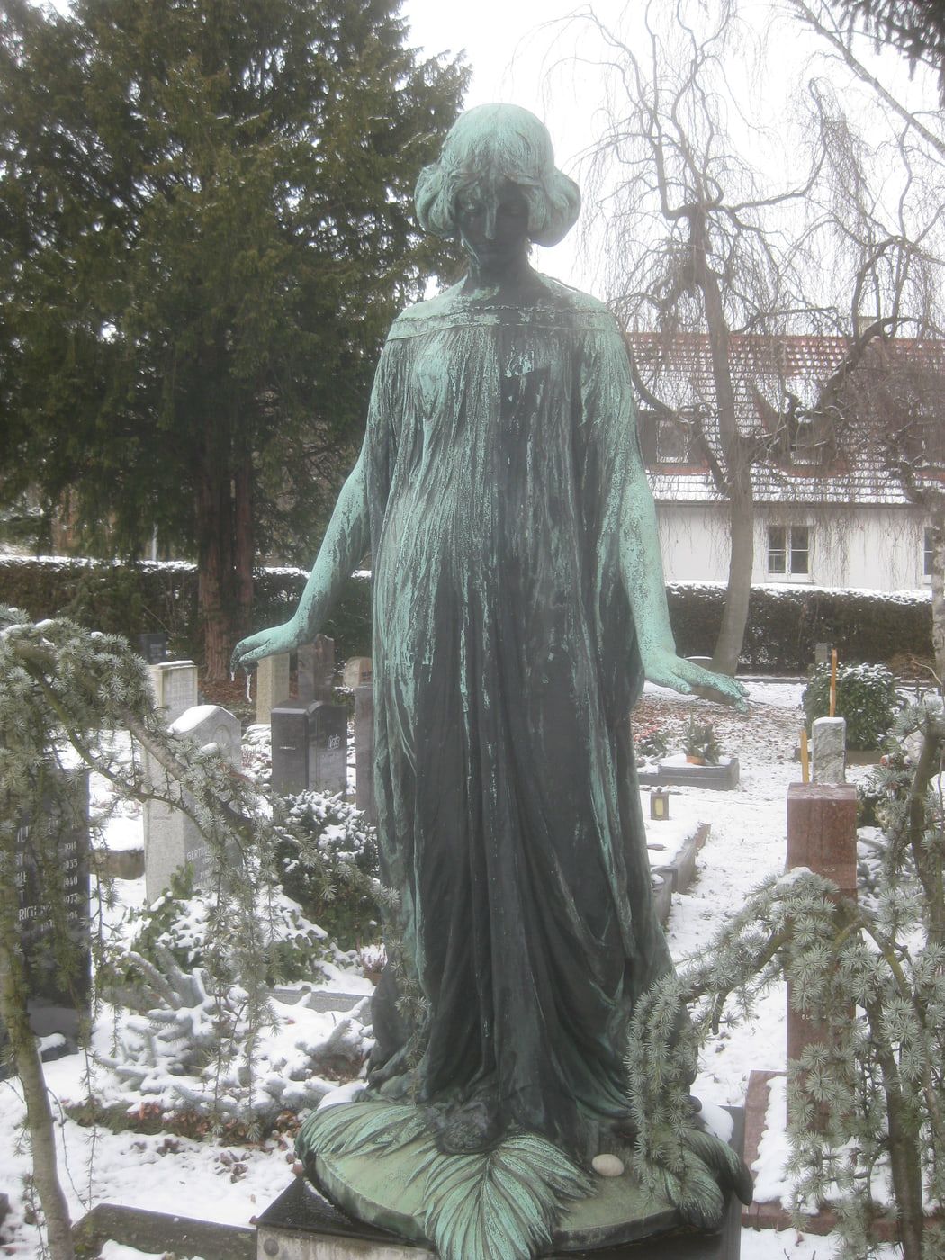 Grün patinierte weibliche Bronzefigur auf einem verschneiten Grab auf Bergfriedhof Stuttgart